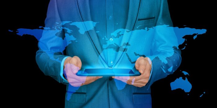 A businessman holding a digital tablet with a world map overlay, representing the global reach and applicability of an internationally recognized management degree